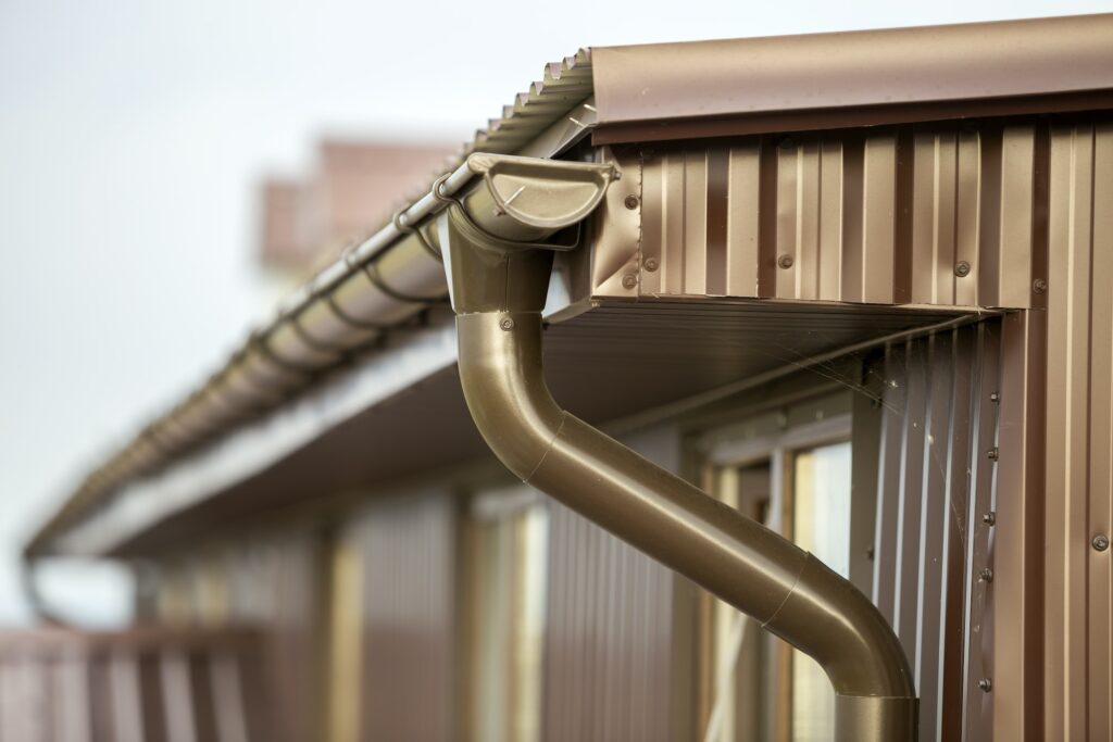 Close-up detail of cottage house corner with metal planks siding and roof with gutter rain system.